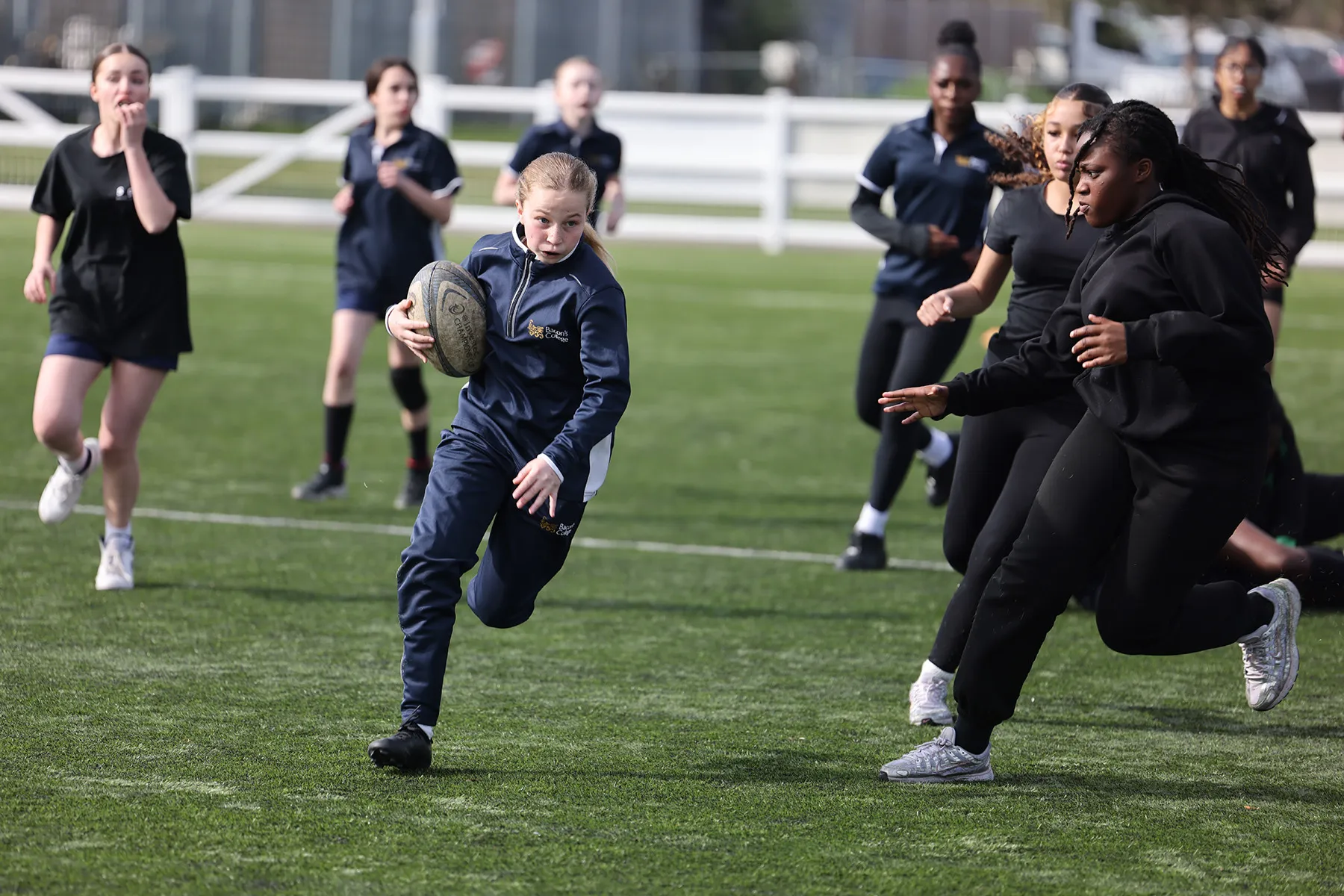 Young girl running with rugby ball, being chased by other young girls.