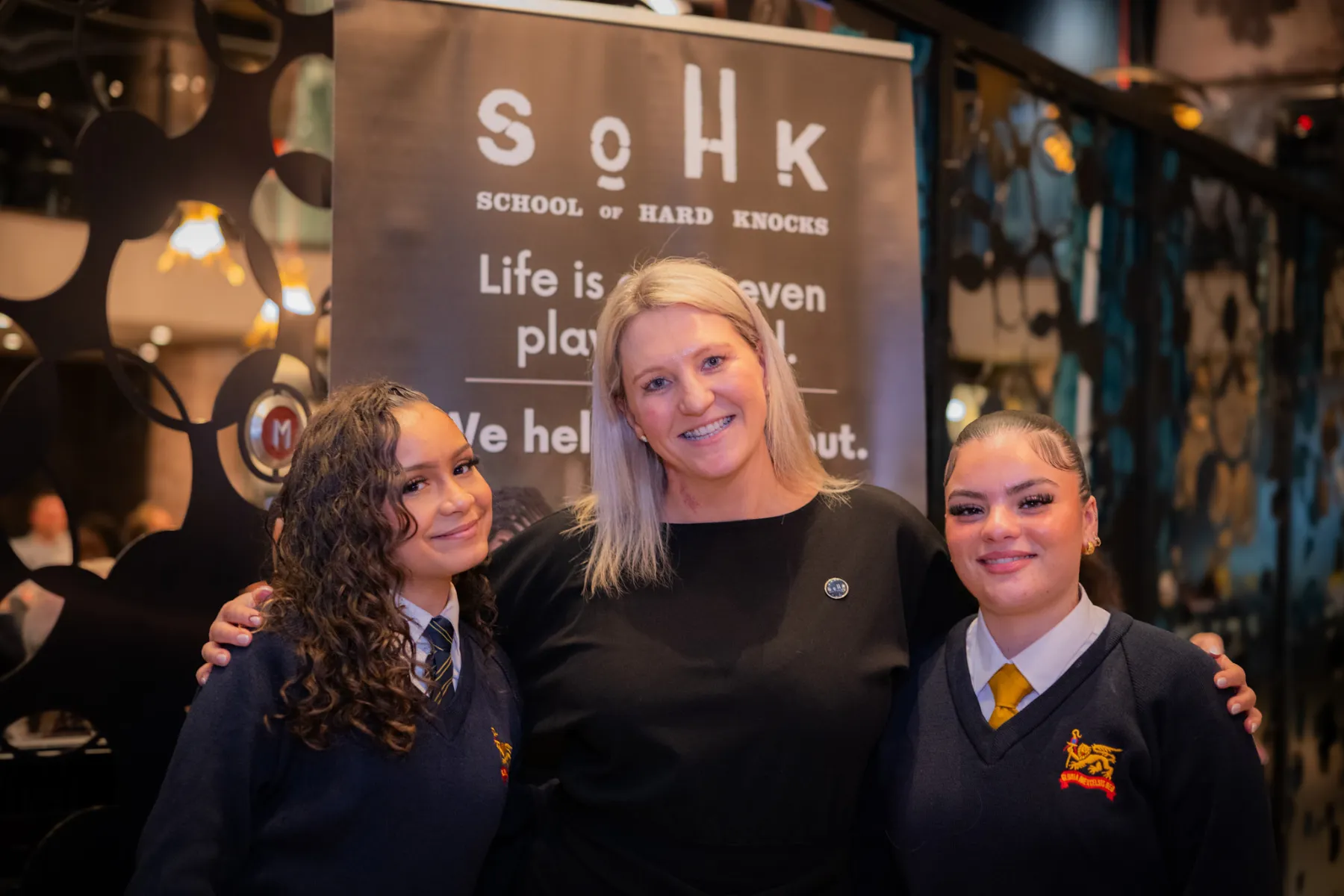 Female SOHK staff member with her arms around two female students, smiling.